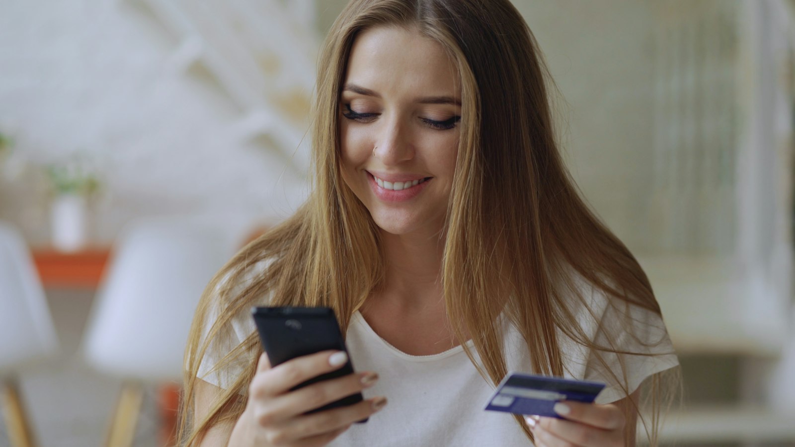 Mujer sonriente con su celular y una tarjeta en la mano